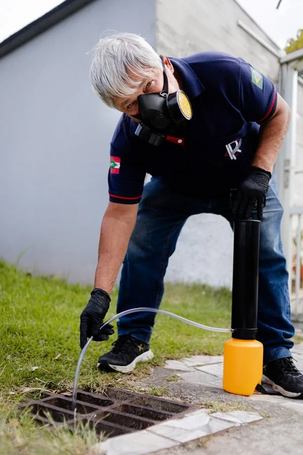 Técnico aplicando dedetização em pó em ralo externo